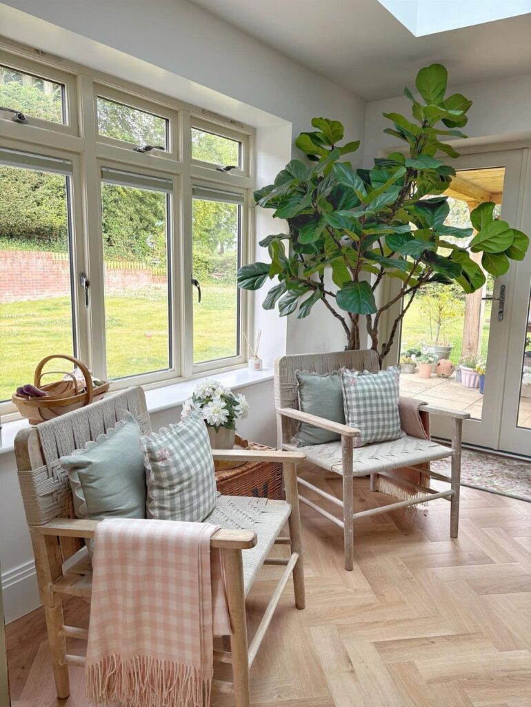 Bright farmhouse living room with light wood floors, sage green pillows, and large plant.
