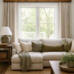 Living room with a wooden beam valance over cream curtains and a beige sofa.